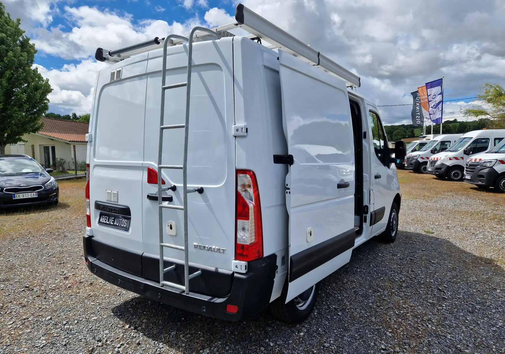 Vue 3/4 arrière droite d’un Renault Master blanc 2019 avec galerie et échelle métallique sur porte arrière.