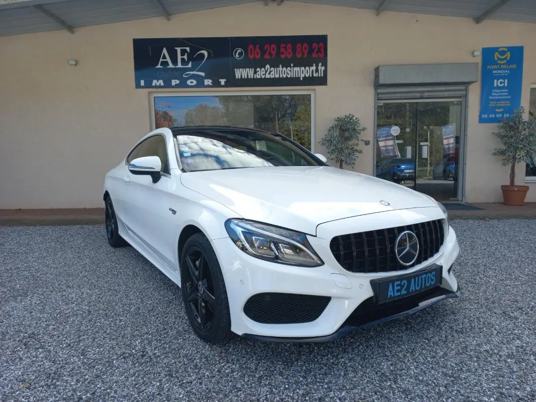 Vue 3/4 avant gauche d'une Mercedes Classe C Coupé blanche avec calandre noire et jantes noires, stationnée devant un garage.