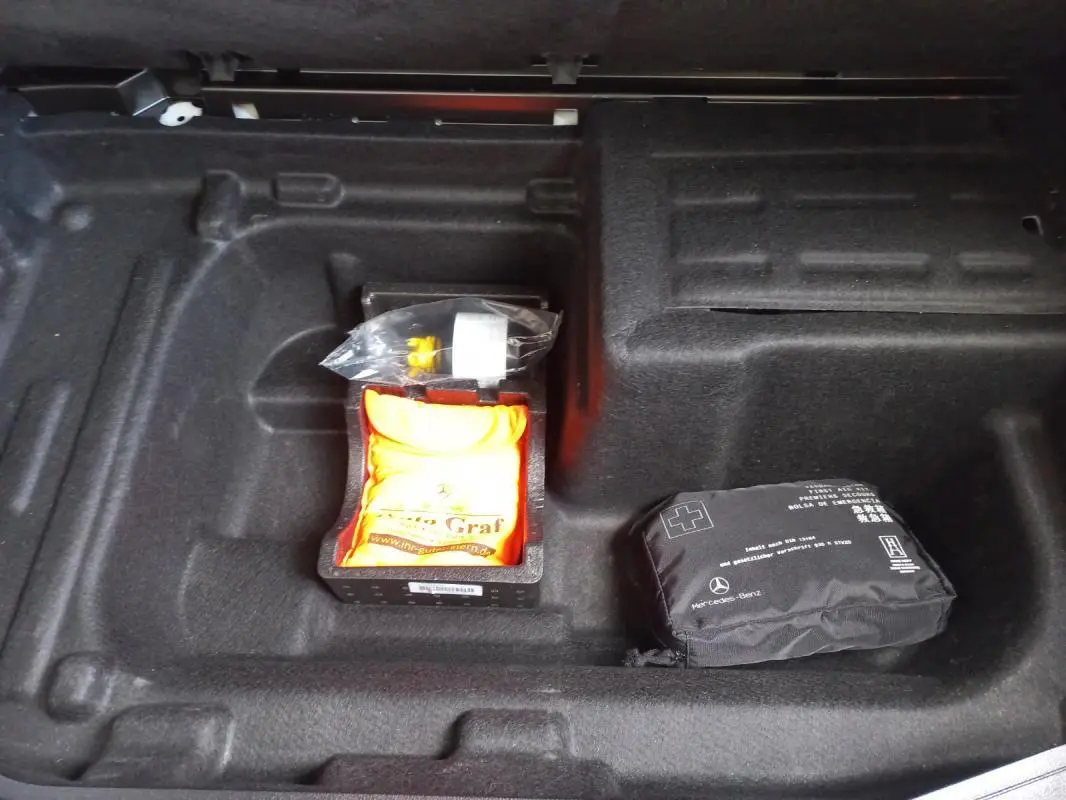 Coffre ouvert d’une Mercedes Classe C Coupé blanc, vue plongeante sur rangement avec trousse de secours et kit de réparation.