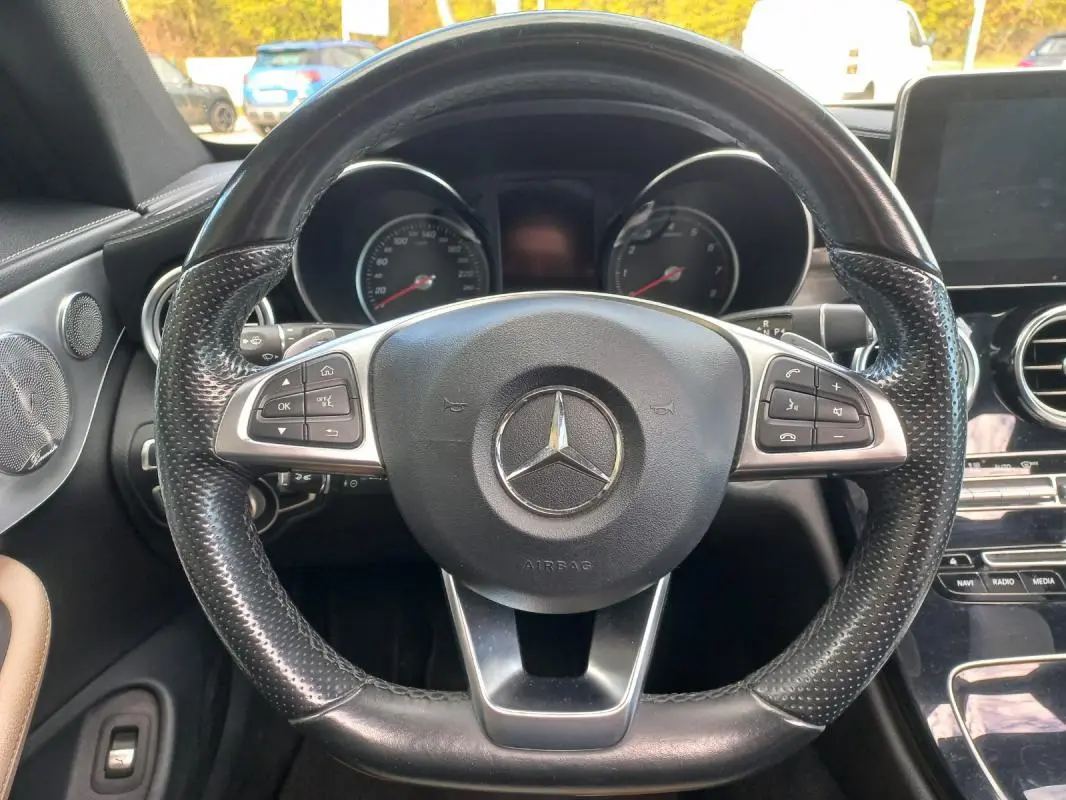 Vue rapprochée du volant cuir noir multifonctions d’une Mercedes Classe C Coupé 2016, tableau de bord et écran central visibles.