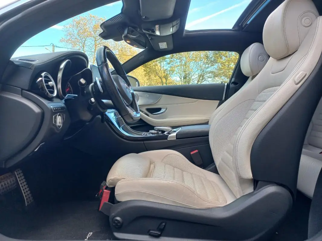 Vue intérieure côté conducteur de la Mercedes Classe C Coupé blanc avec sièges cuir beige et toit ouvrant panoramique.