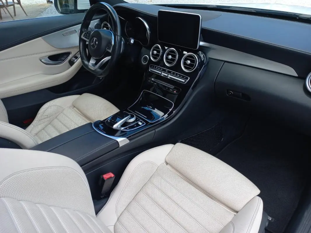 Vue intérieure côté conducteur de la Mercedes Classe C Coupé 2016, sièges cuir beige et tableau de bord noir brillant.