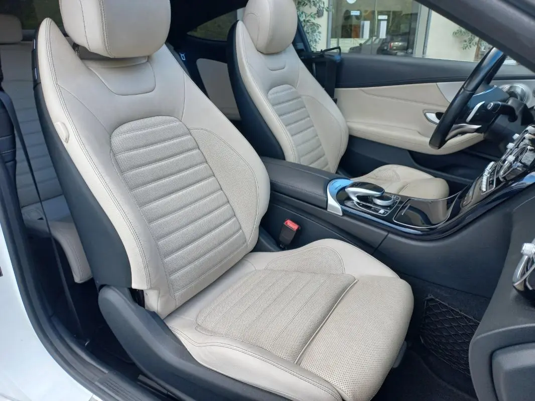 Vue intérieure côté conducteur montrant les sièges en cuir beige et la console centrale noire brillante d'une Mercedes Classe C Coupé blanche.