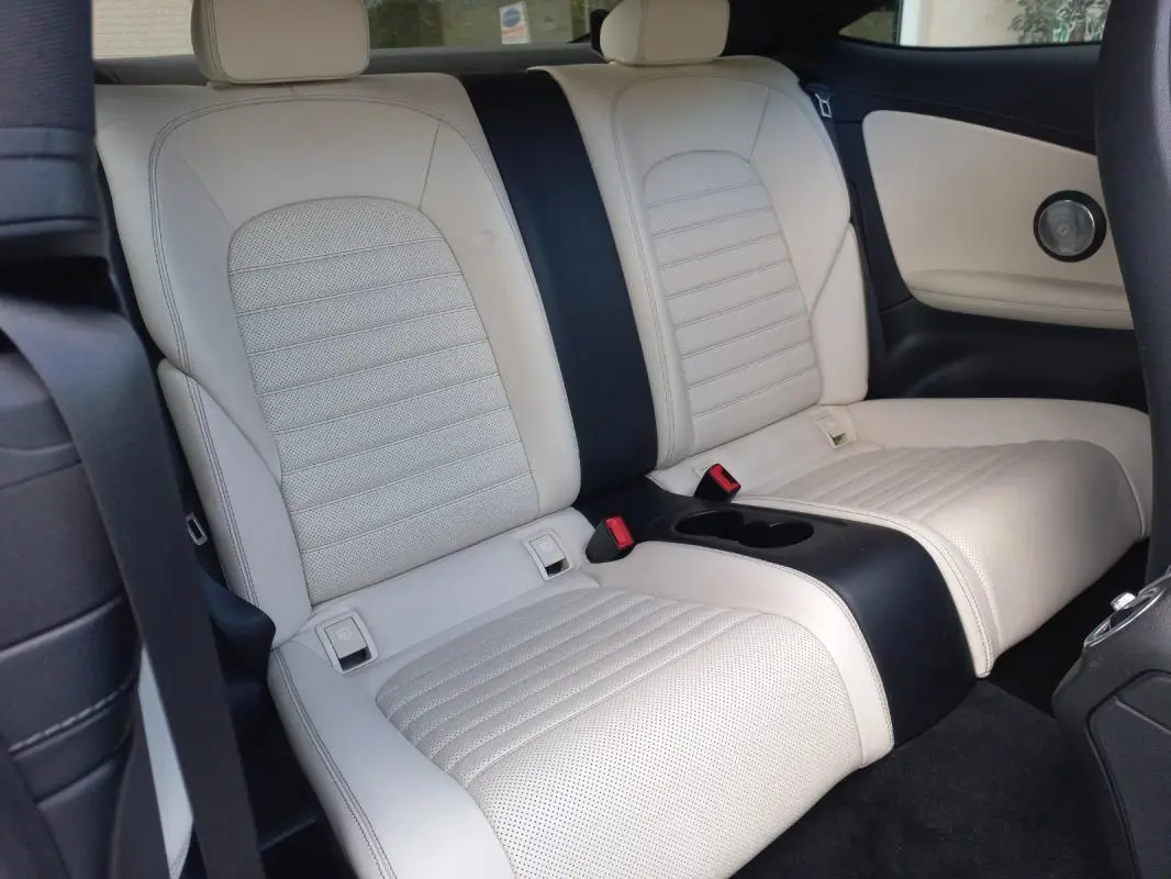 Vue intérieure arrière montrant les sièges en cuir beige clair avec accoudoir central et ceinture noire d'une Mercedes Classe C Coupé.