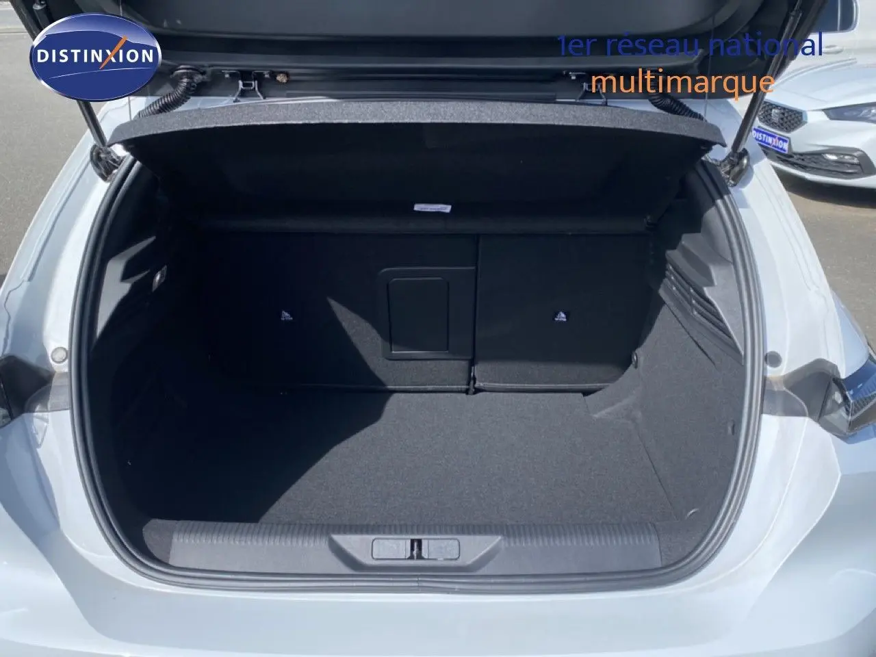 Coffre ouvert vu de l'arrière d'une Peugeot 308 Hybrid 145ch GT blanc Okenite, espace de chargement vide et propre.
