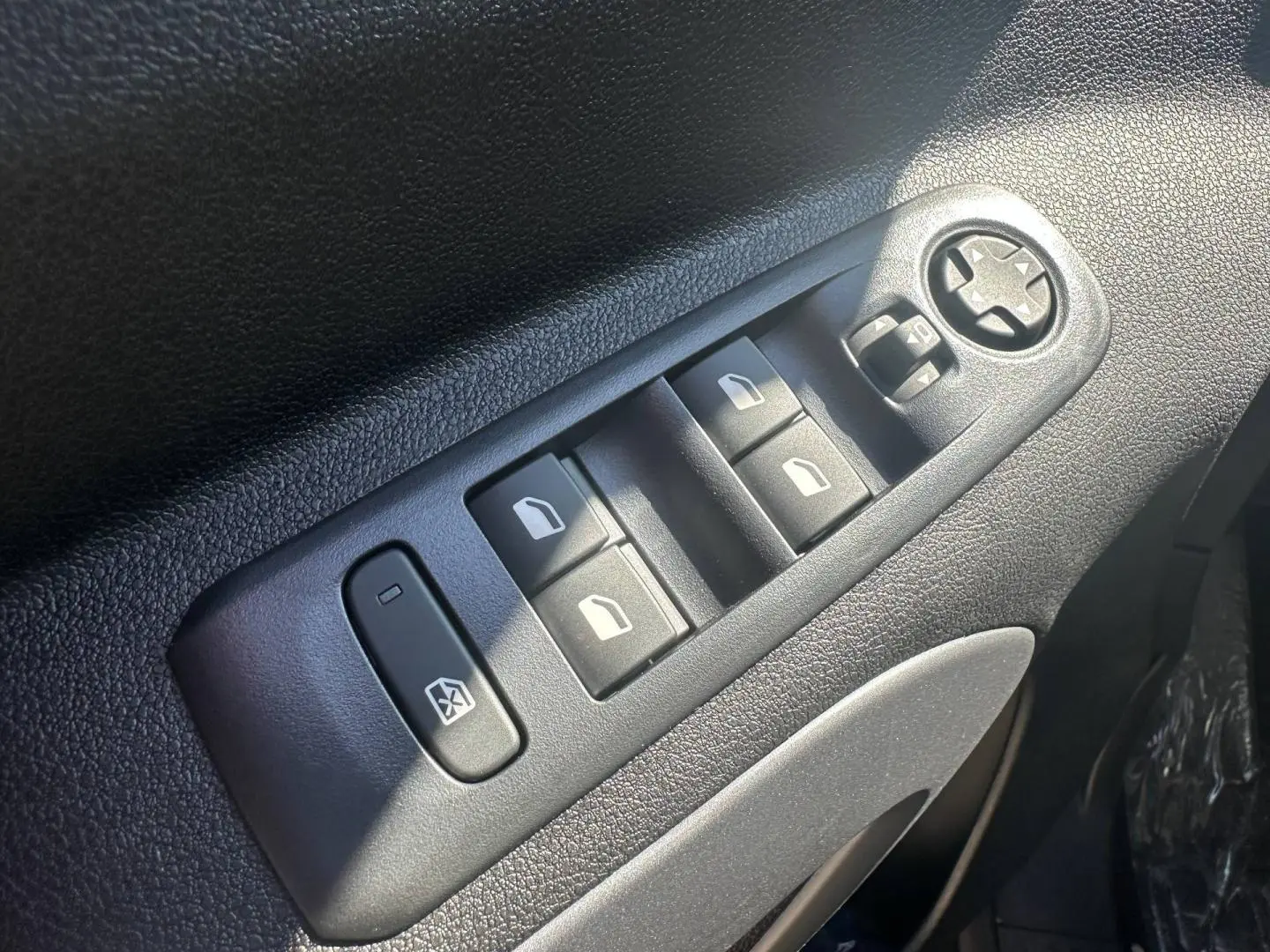 Gros plan sur les commandes des vitres électriques et réglage des rétroviseurs côté conducteur du Citroën Berlingo Sirkka Green.