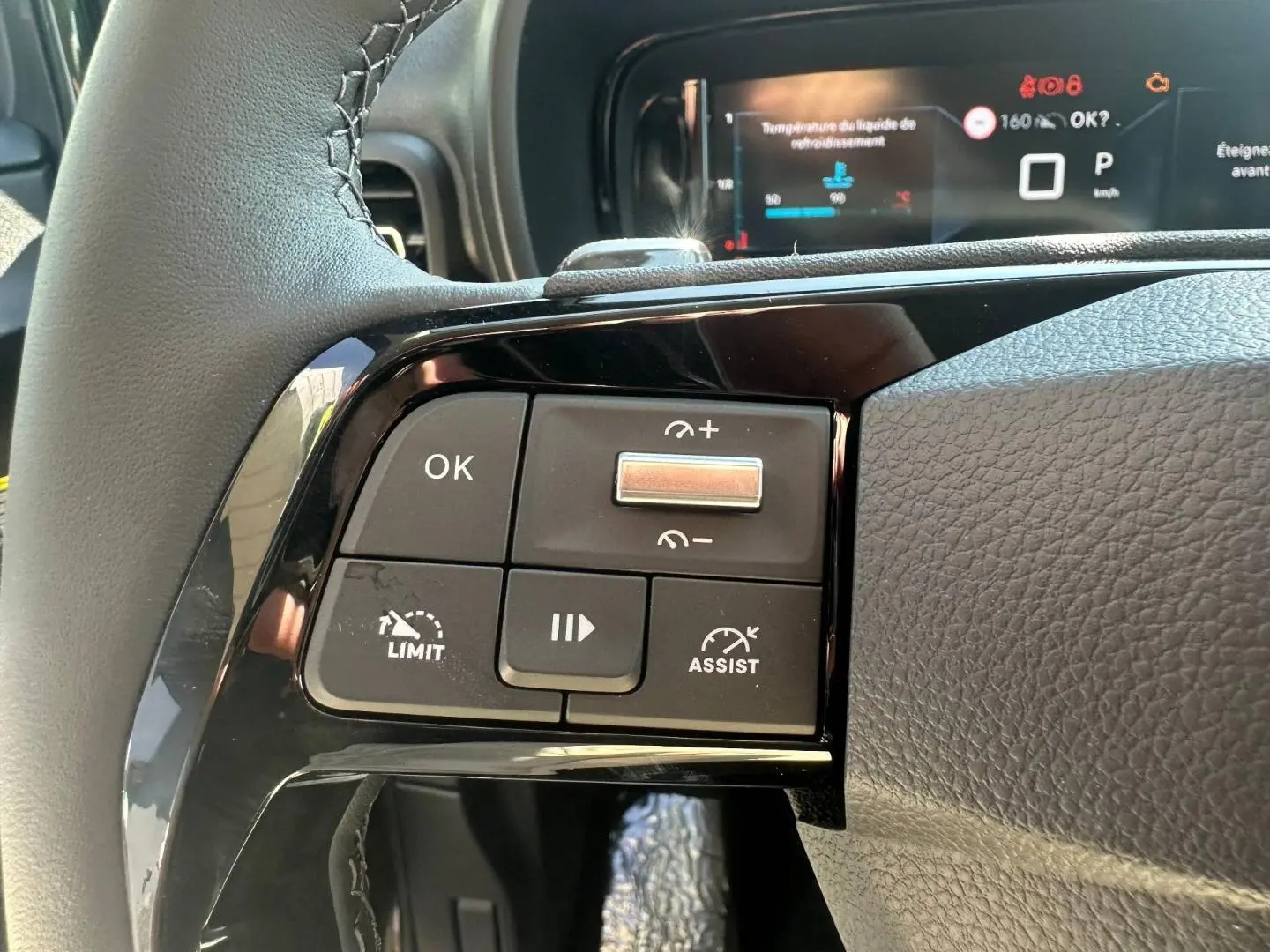 Gros plan sur les commandes au volant côté gauche du Citroën Berlingo 2026 en Sirkka Green, affichage numérique en arrière-plan.