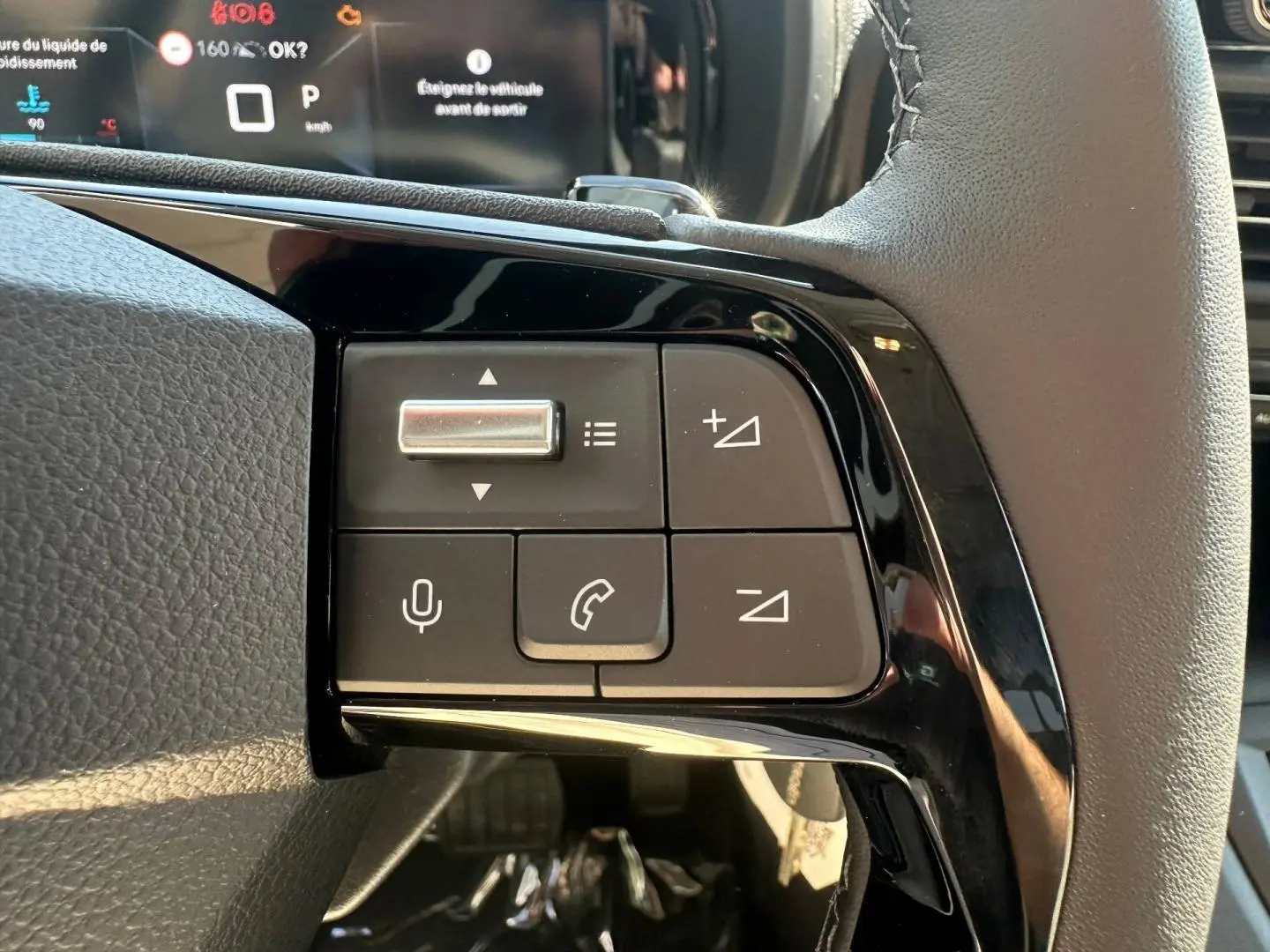 Gros plan sur les commandes au volant cuir noir du Citroën Berlingo 2026, version Sirkka Green, avec affichage numérique en arrière-plan.