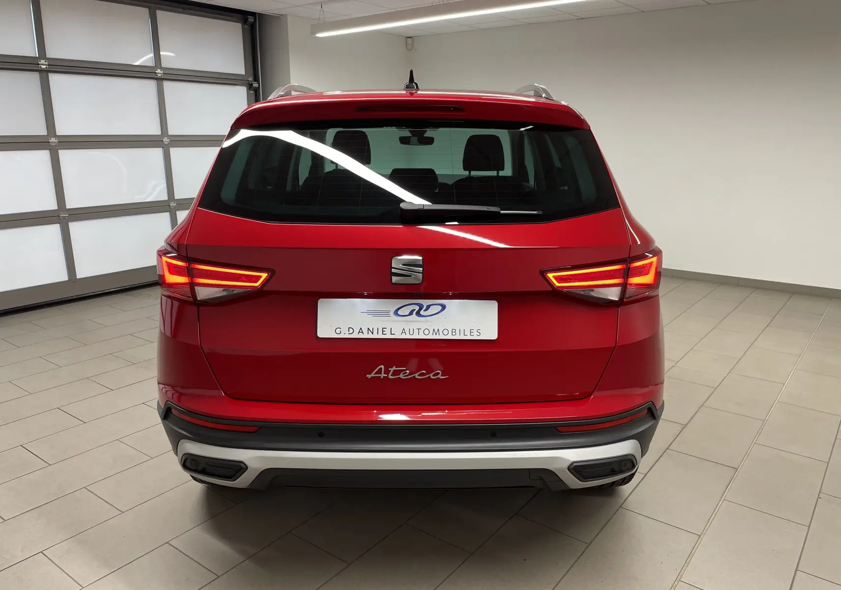 Vue arrière du SUV SEAT Ateca 2024 en Rouge Velvet métallisé avec feux allumés dans un garage intérieur.