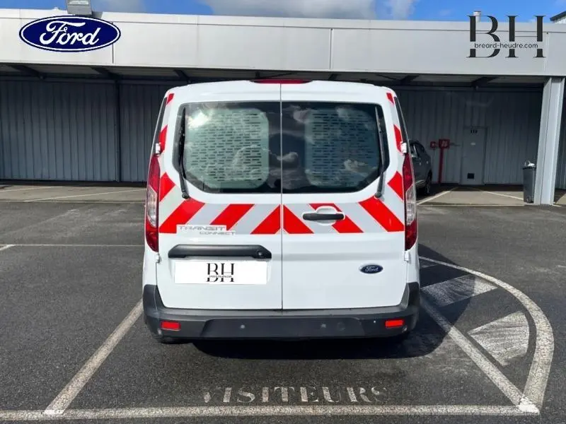 Vue arrière d'un Ford Transit Connect blanc glacier avec bandes rouges réfléchissantes, portes vitrées et pare-chocs noirs.