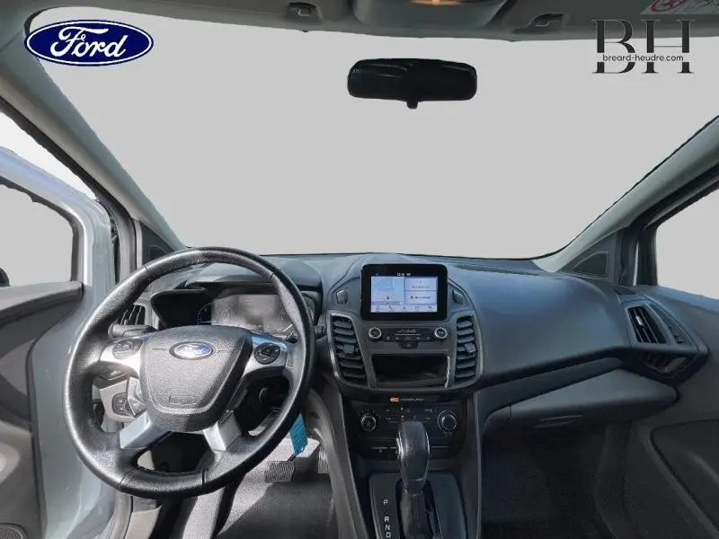 Vue intérieure avant du Ford Transit Connect blanc glacier, mettant en valeur le tableau de bord avec écran GPS et volant multifonction.