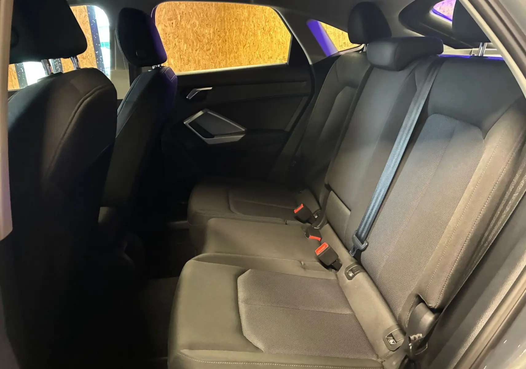 Vue intérieure côté droit des sièges arrière noirs d'un Audi Q3 Sportback gris, avec ceintures et appuie-têtes visibles.
