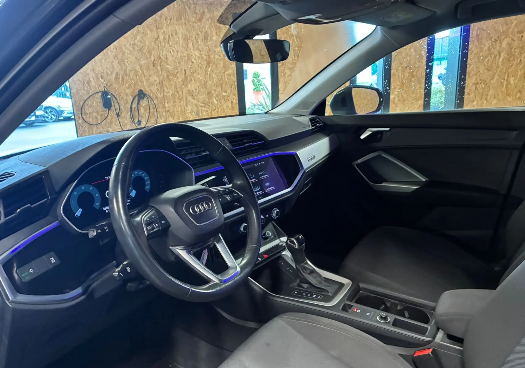 Vue intérieure côté conducteur de l'Audi Q3 Sportback gris, avec tableau de bord numérique et éclairage d'ambiance violet.