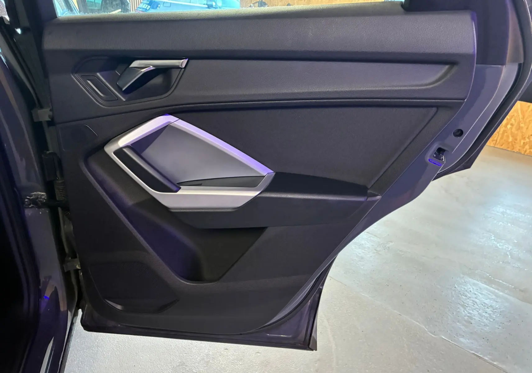 Vue intérieure de la porte arrière gauche gris foncé de l'Audi Q3 Sportback avec poignée argentée et accoudoir intégré.