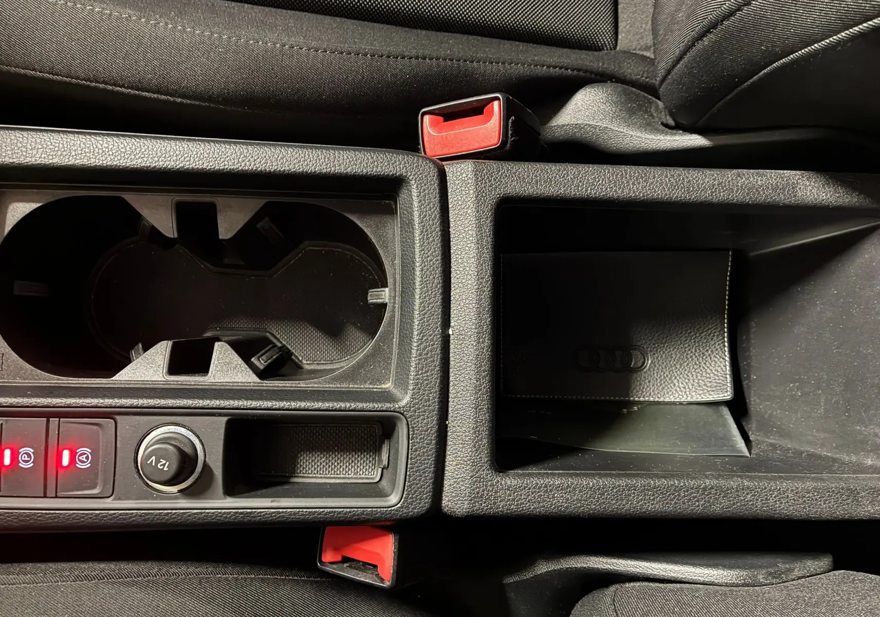 Vue rapprochée de la console centrale noire de l'Audi Q3 Sportback avec porte-gobelets et rangement à côté du frein à main électrique.