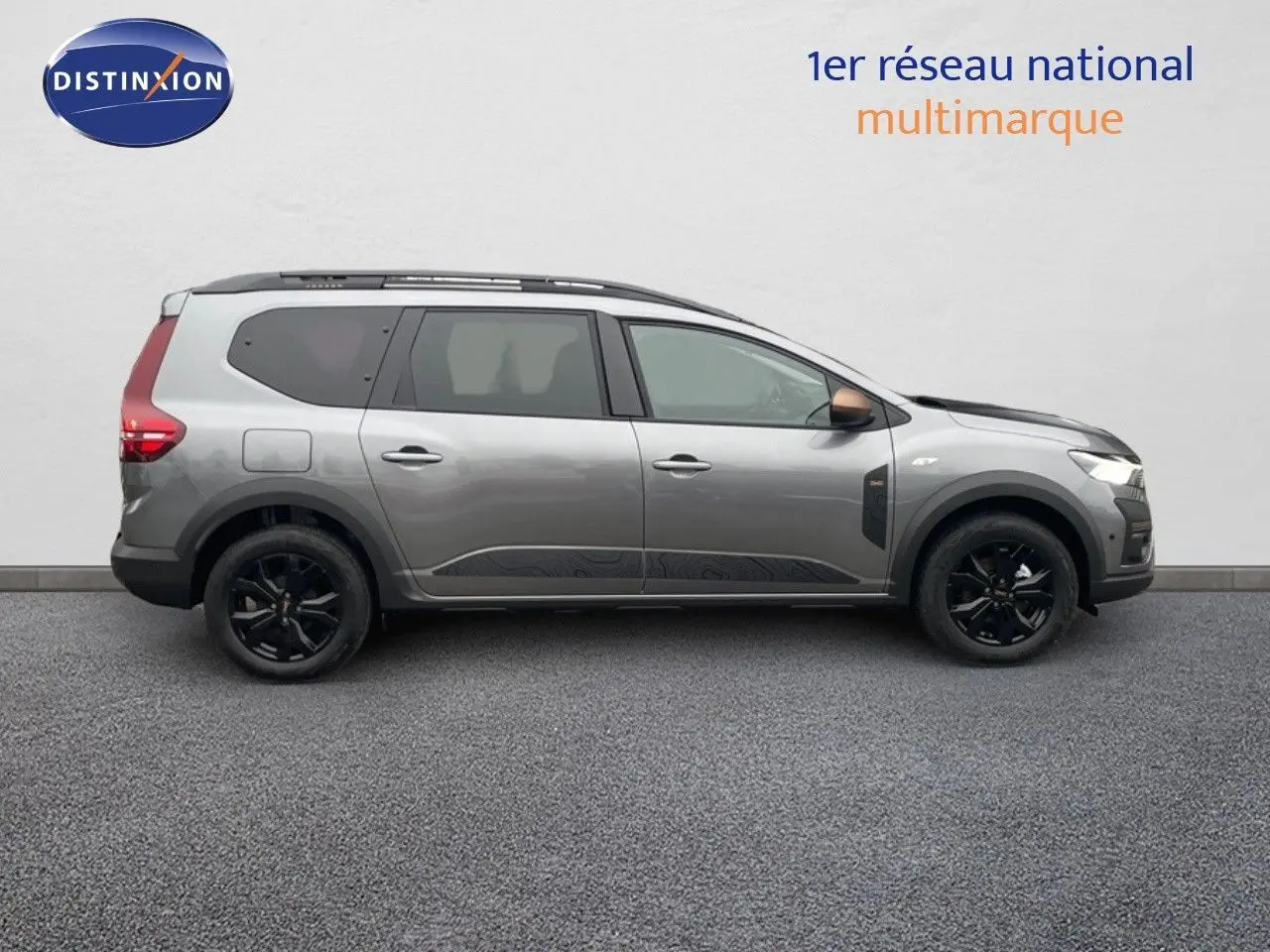 Vue de profil côté droit d'un Dacia Jogger gris schiste métal, avec jantes noires et toit équipé de barres de toit.