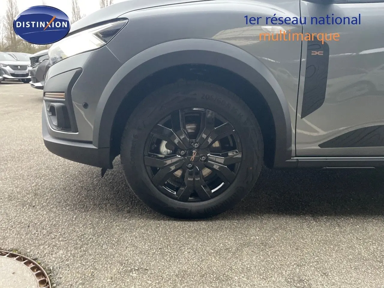 Gros plan sur la roue avant droite d’un Dacia Jogger gris schiste métal, avec jante noire et logo DC sur l’aile.