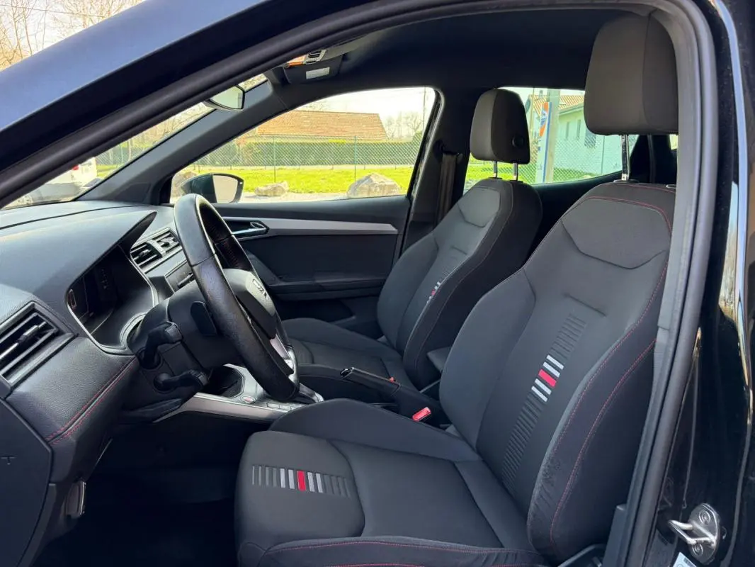 Vue intérieure côté conducteur du SEAT Arona noir 2020, mettant en valeur les sièges sport avec surpiqûres rouges et détails colorés.