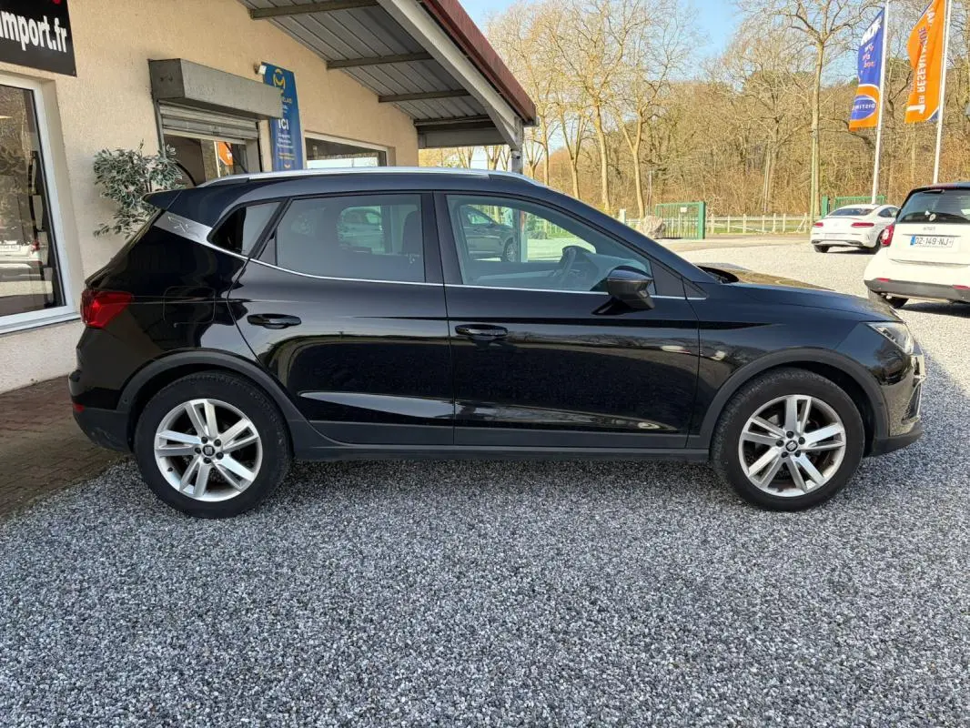 SEAT Arona noir vue de profil côté gauche, avec jantes alliage et toit ouvrant, stationné sur gravier devant un bâtiment.