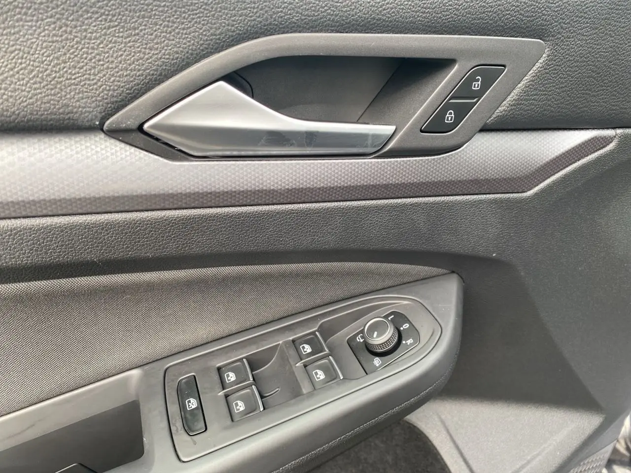 Détail de la porte côté conducteur d'une Volkswagen Golf VIII noire, avec commandes des vitres et serrure intégrée.