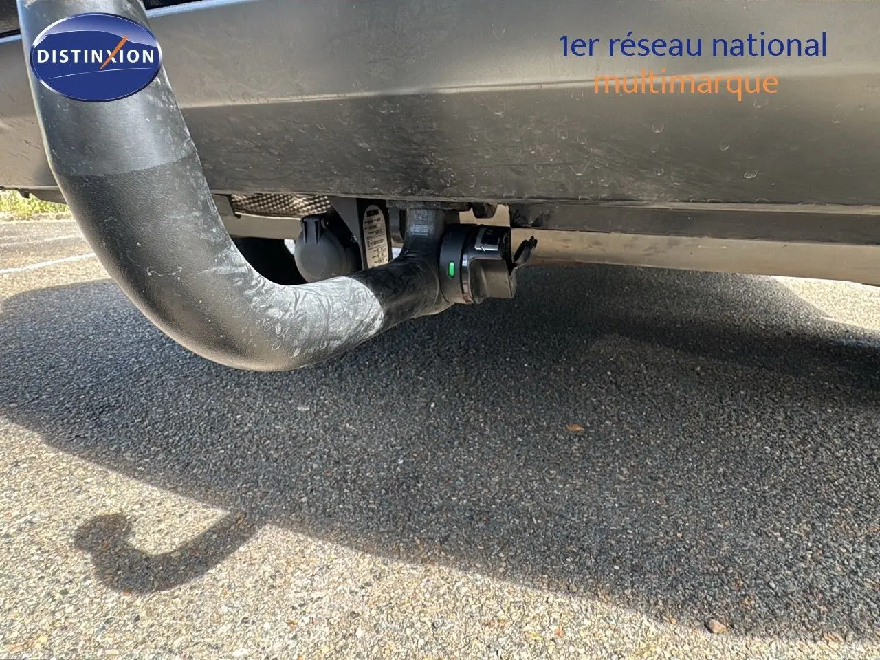 Gros plan sous le pare-chocs arrière d'une Renault Rafale blanc satin avec attelage visible sur fond de bitume.