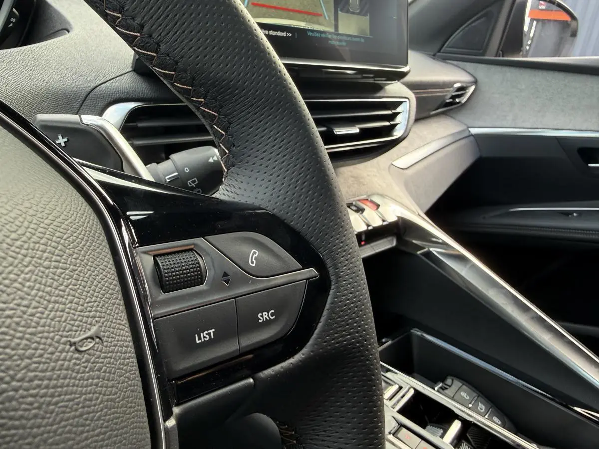Gros plan sur le volant cuir perforé et la console centrale grise Alcantara du Peugeot 3008 Hybrid 2023.