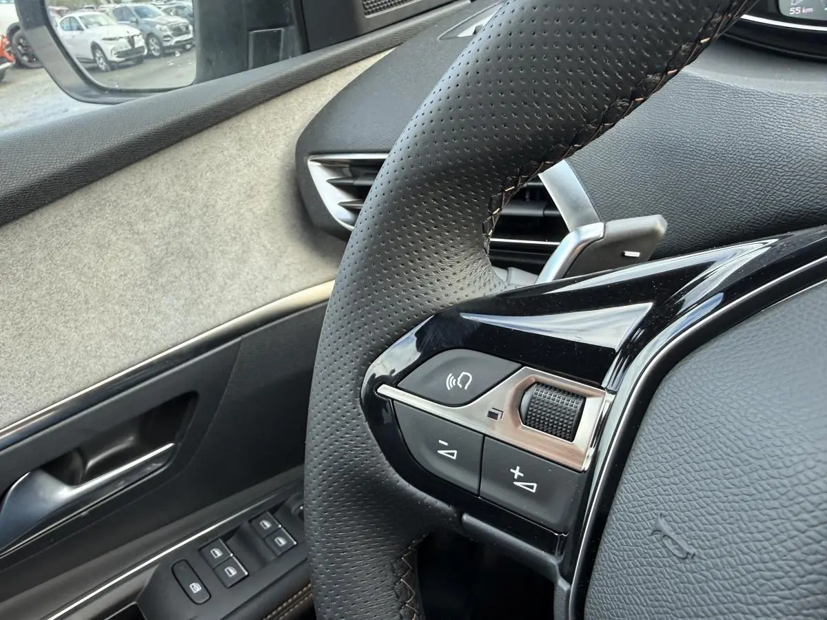 Gros plan sur le volant cuir perforé et la portière côté conducteur du Peugeot 3008 Hybrid gris, intérieur Alcantara.