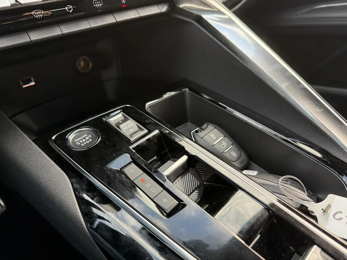 Gros plan sur la console centrale noire brillante du Peugeot 3008 Hybrid 2023 avec bouton start, sélecteur de mode et clé électronique.