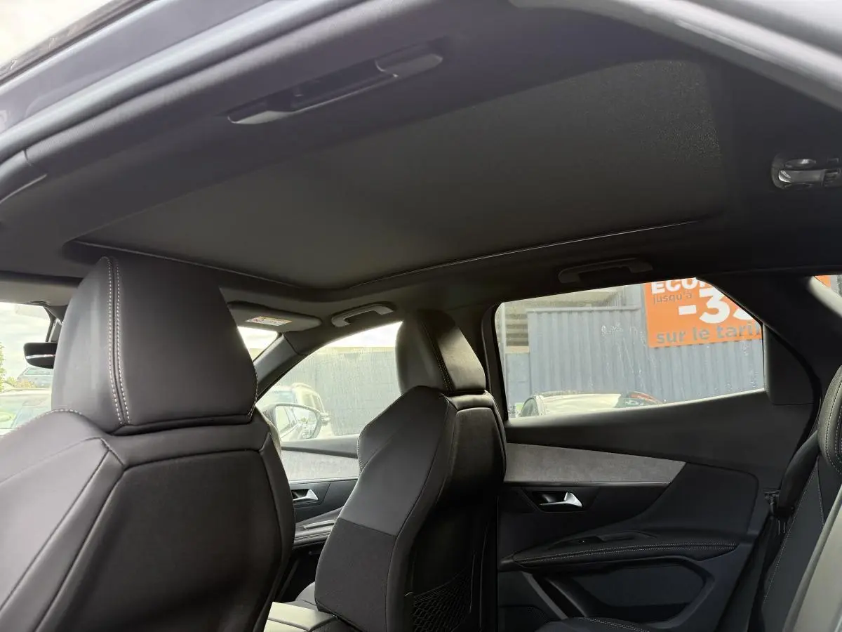 Vue intérieure côté droit du Peugeot 3008 Hybrid 2023 avec sièges en cuir noir et toit ouvrant panoramique fermé.