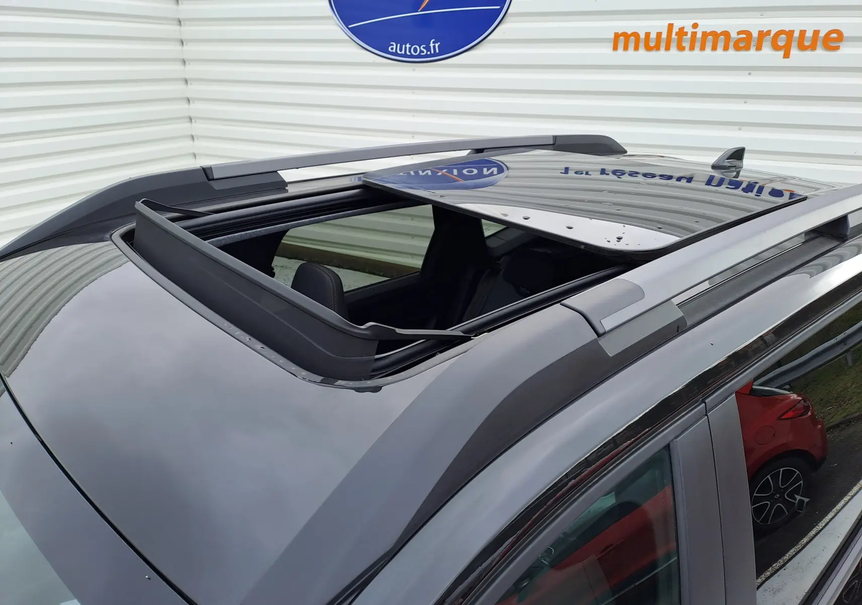 Toit ouvrant panoramique ouvert vu en plongée sur un Dacia Bigster noir nacré avec barres de toit grises.