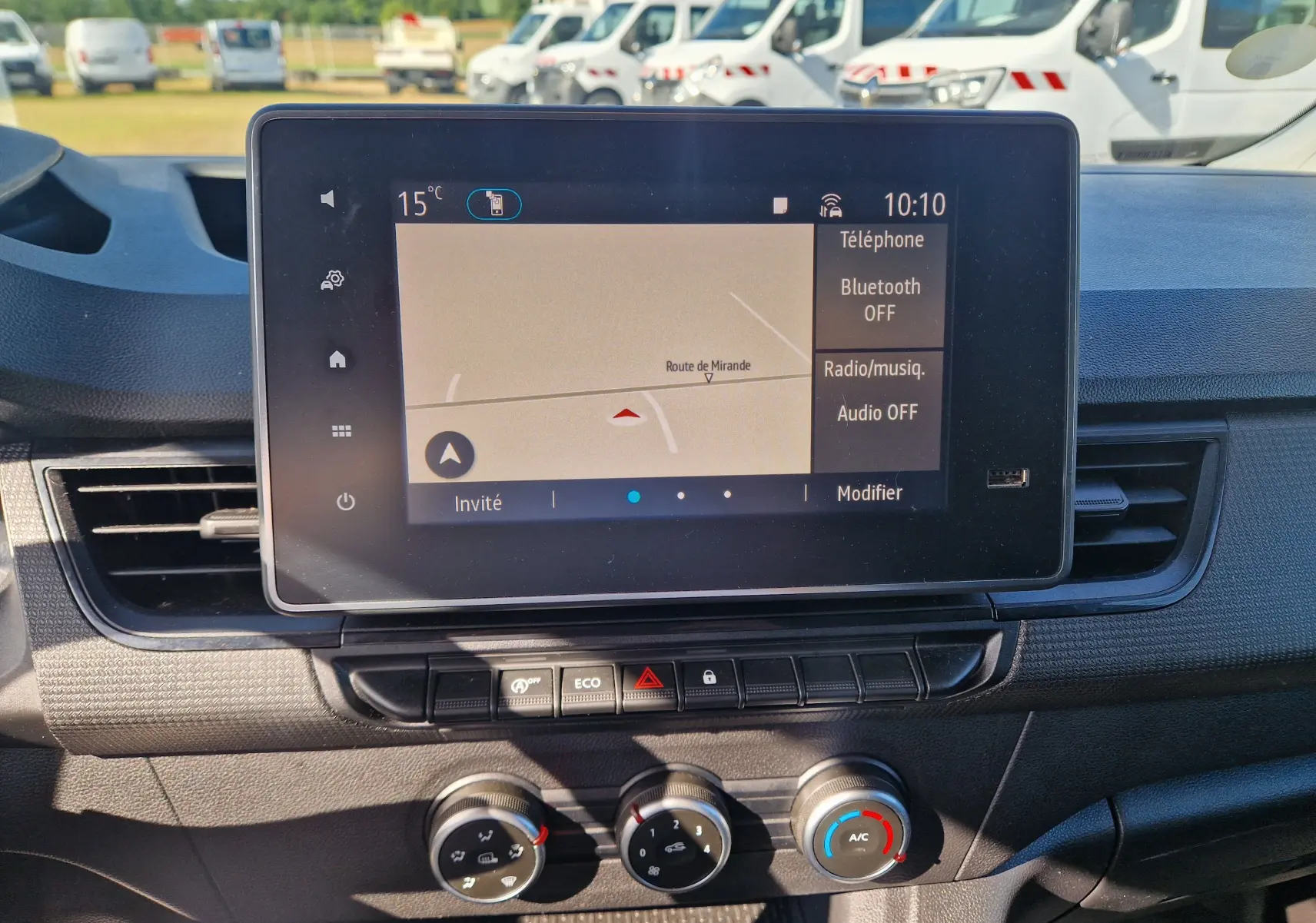 Vue rapprochée de l’écran tactile central et des commandes de climatisation du Renault Kangoo blanc 2023, intérieur fonctionnel.
