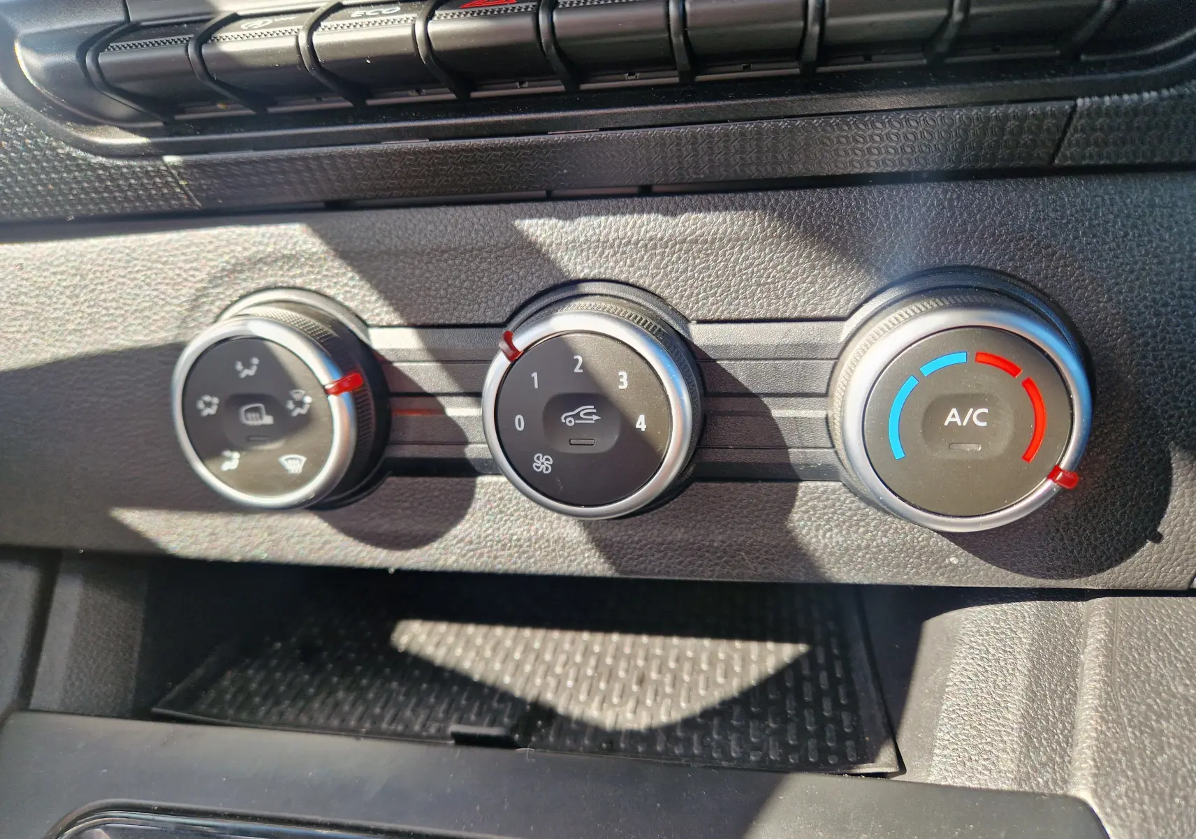Gros plan sur les commandes de climatisation du Renault Kangoo blanc 2023, avec réglages manuels et boutons ronds.