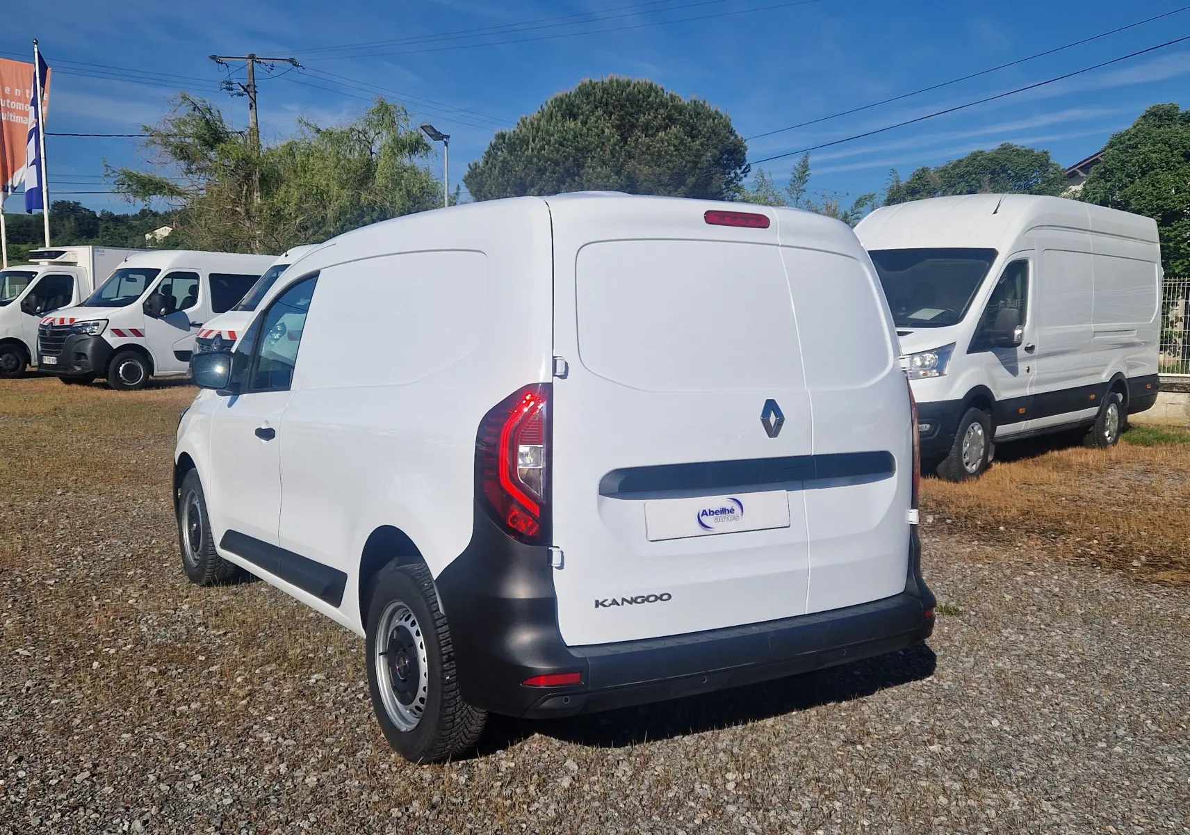 Vue 3/4 arrière droite d’un Renault Kangoo blanc utilitaire avec hayon fermé sur un parking extérieur.