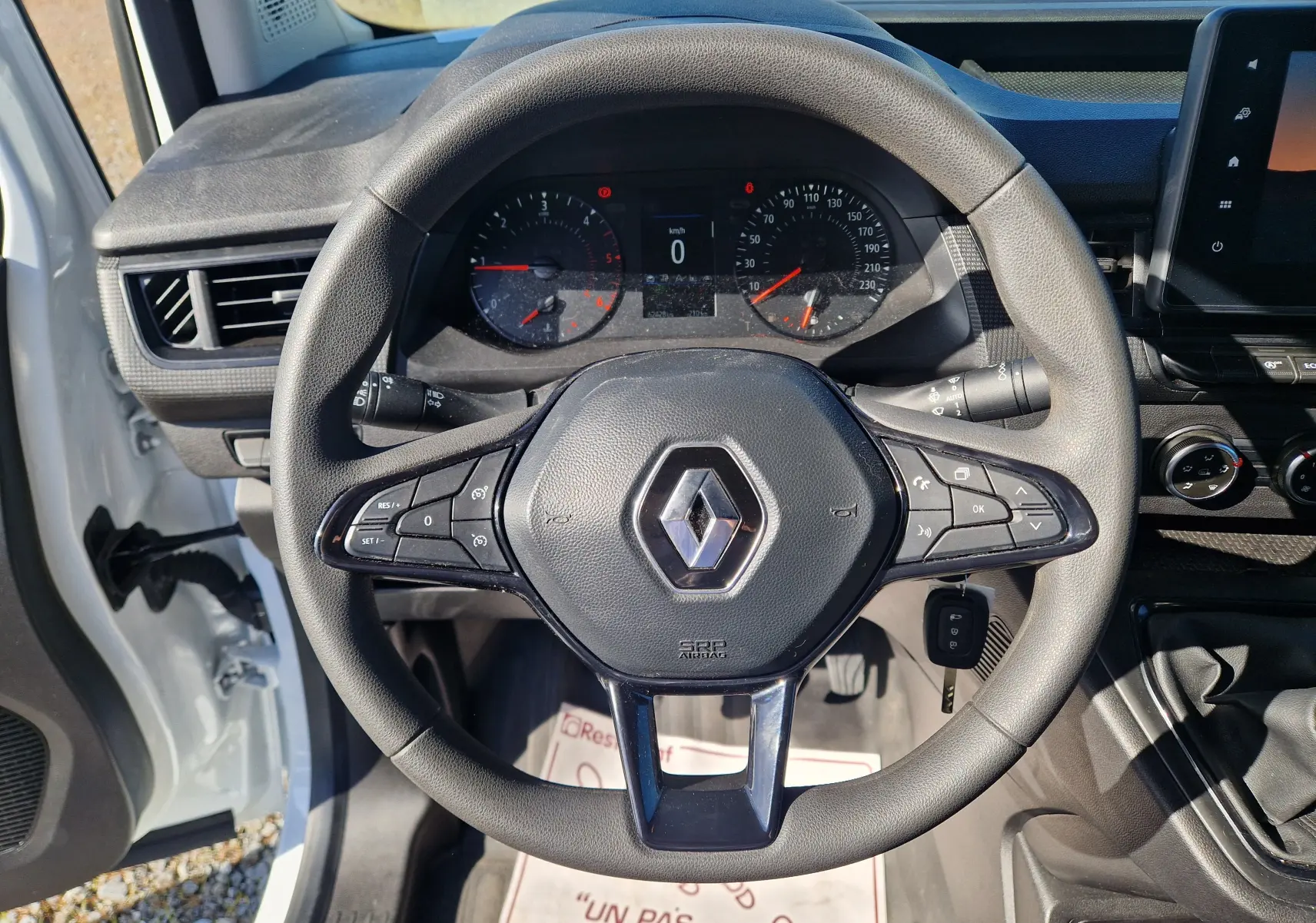 Vue rapprochée du volant noir du Renault Kangoo blanc 2023, avec commandes intégrées et tableau de bord visible.