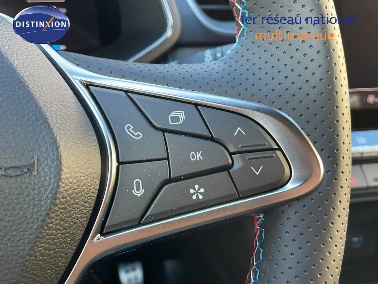 Gros plan sur les commandes multifonctions du volant en cuir noir perforé avec surpiqûres bleues et rouges du Renault Captur E-Tech.