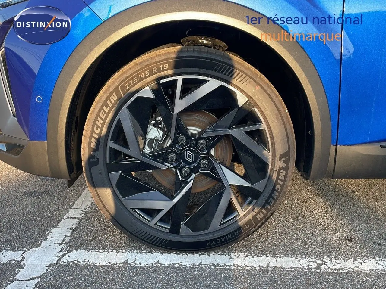 Gros plan sur la roue avant gauche du Renault Captur bleu Iron Metal avec jante noire au design géométrique.