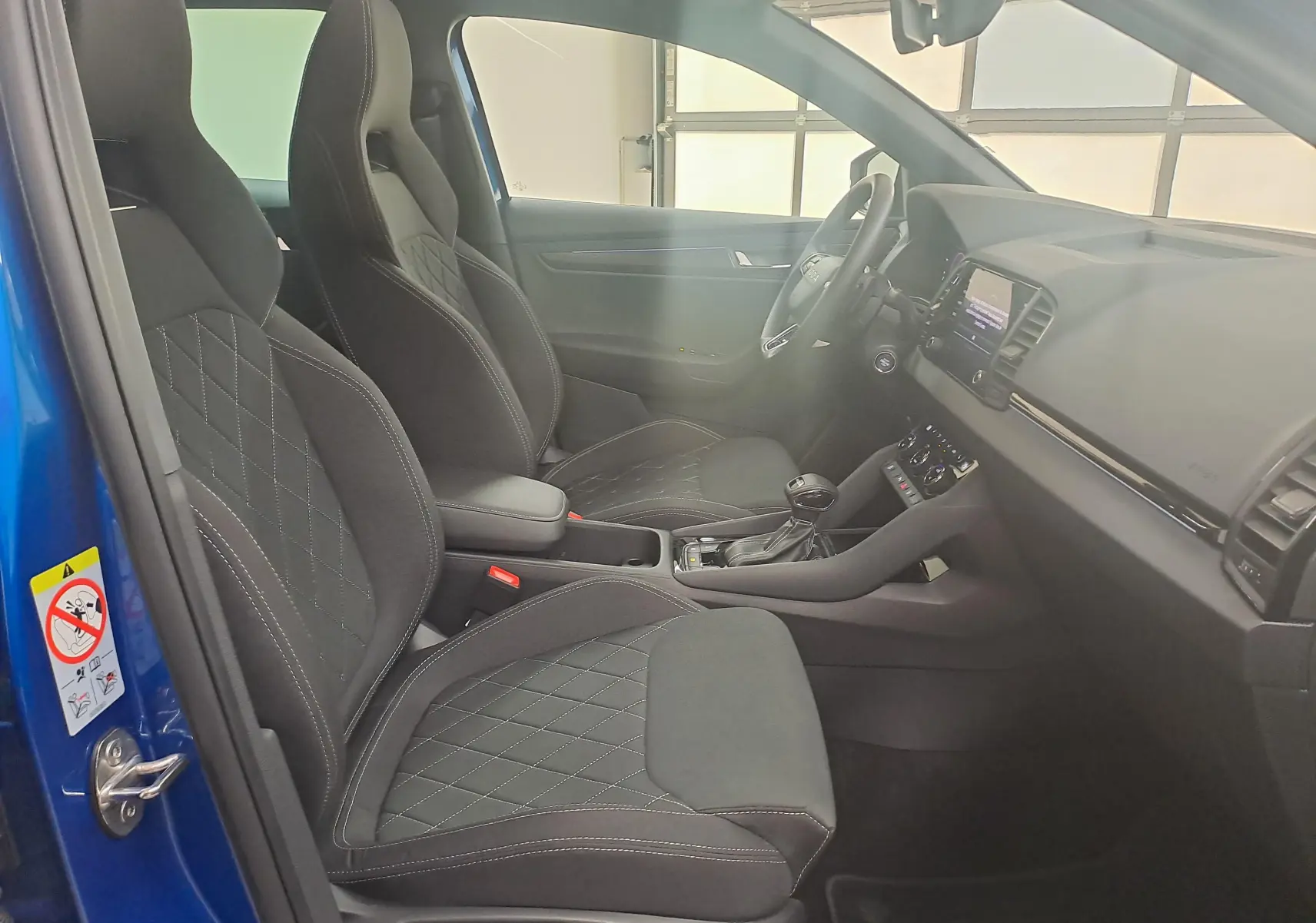Vue intérieure côté gauche du Skoda Karoq Bleu RS 2025, sièges sport noirs avec surpiqûres et console centrale moderne.