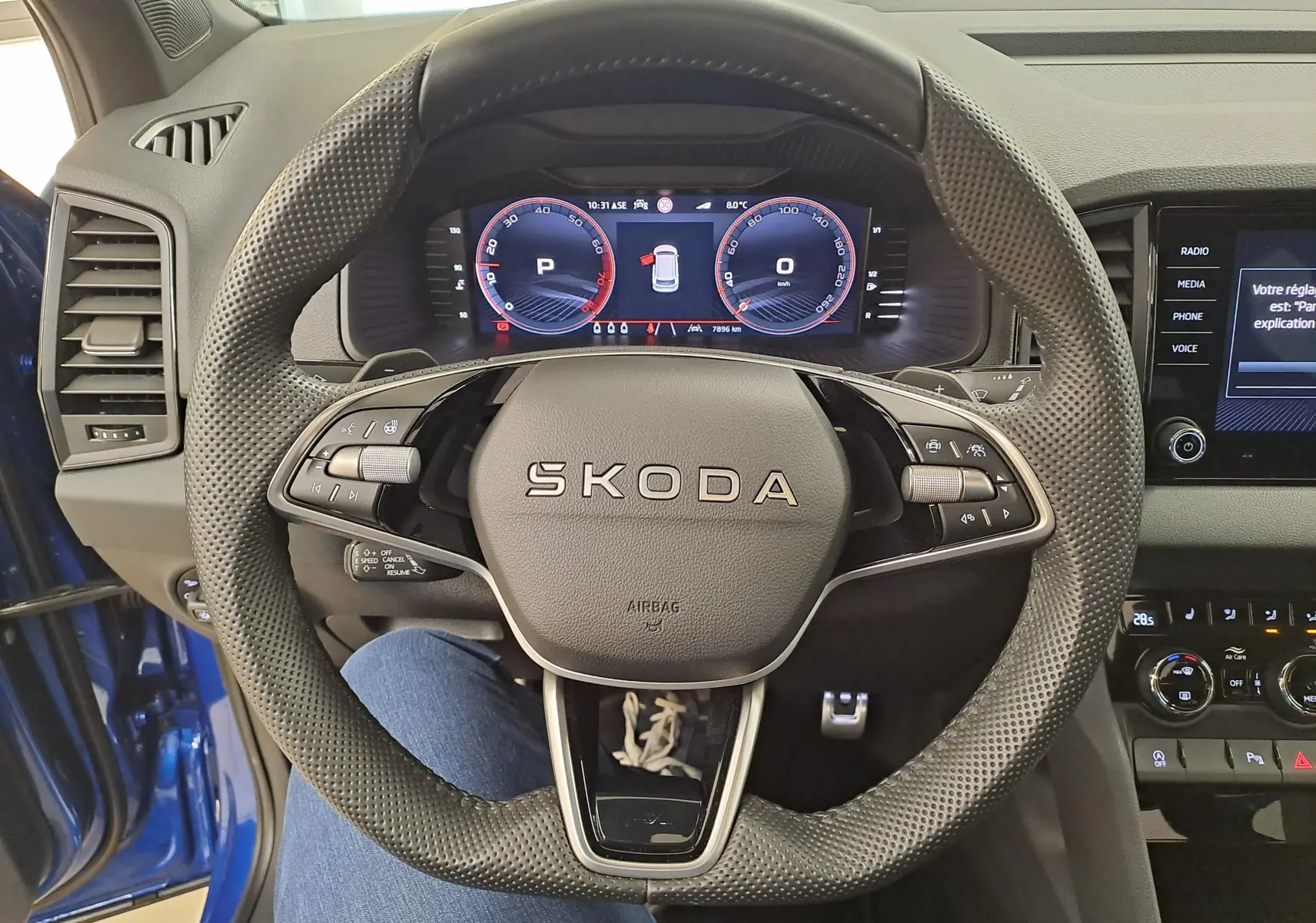 Vue centrée sur le volant perforé SKODA d'un Karoq Bleu RS 2025 avec tableau de bord numérique et console tactile.