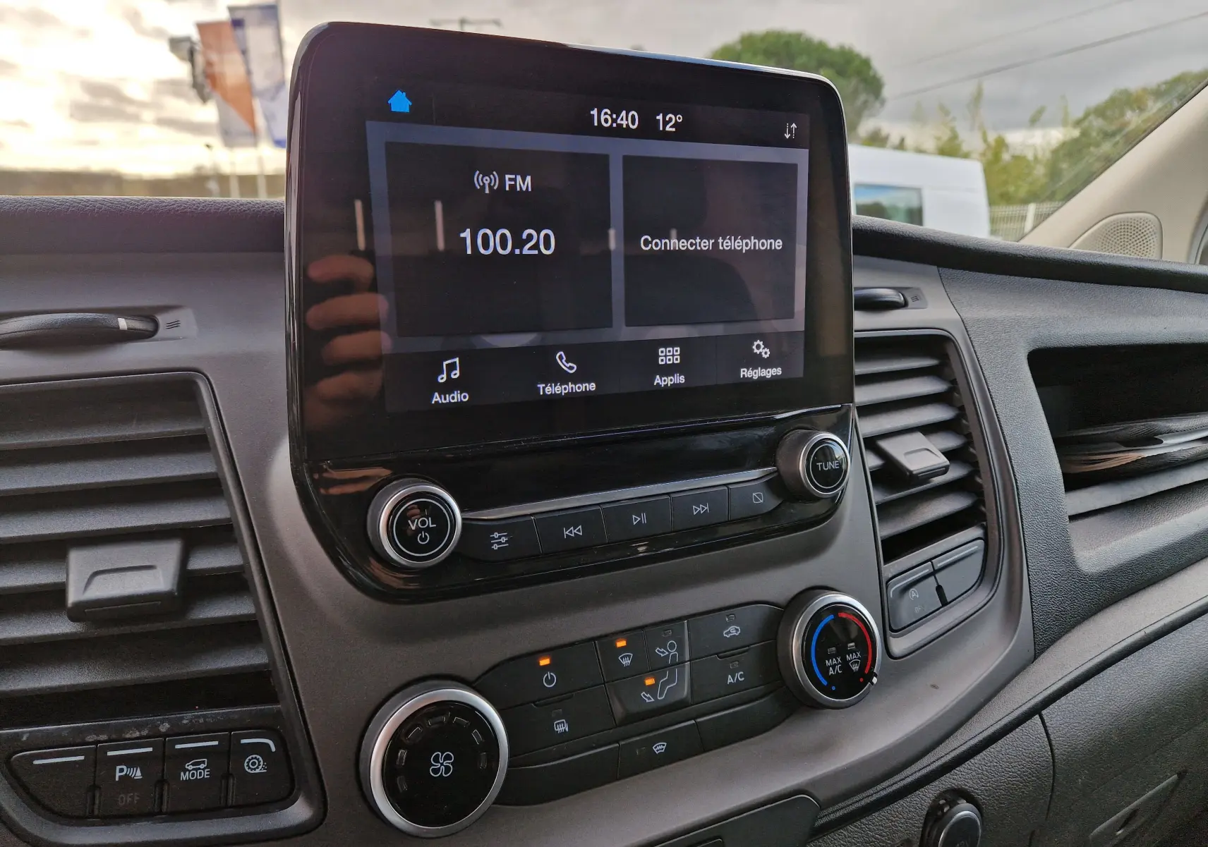 Vue intérieure du tableau de bord du Ford Transit Custom blanc, avec écran tactile central et commandes climatisation visibles.