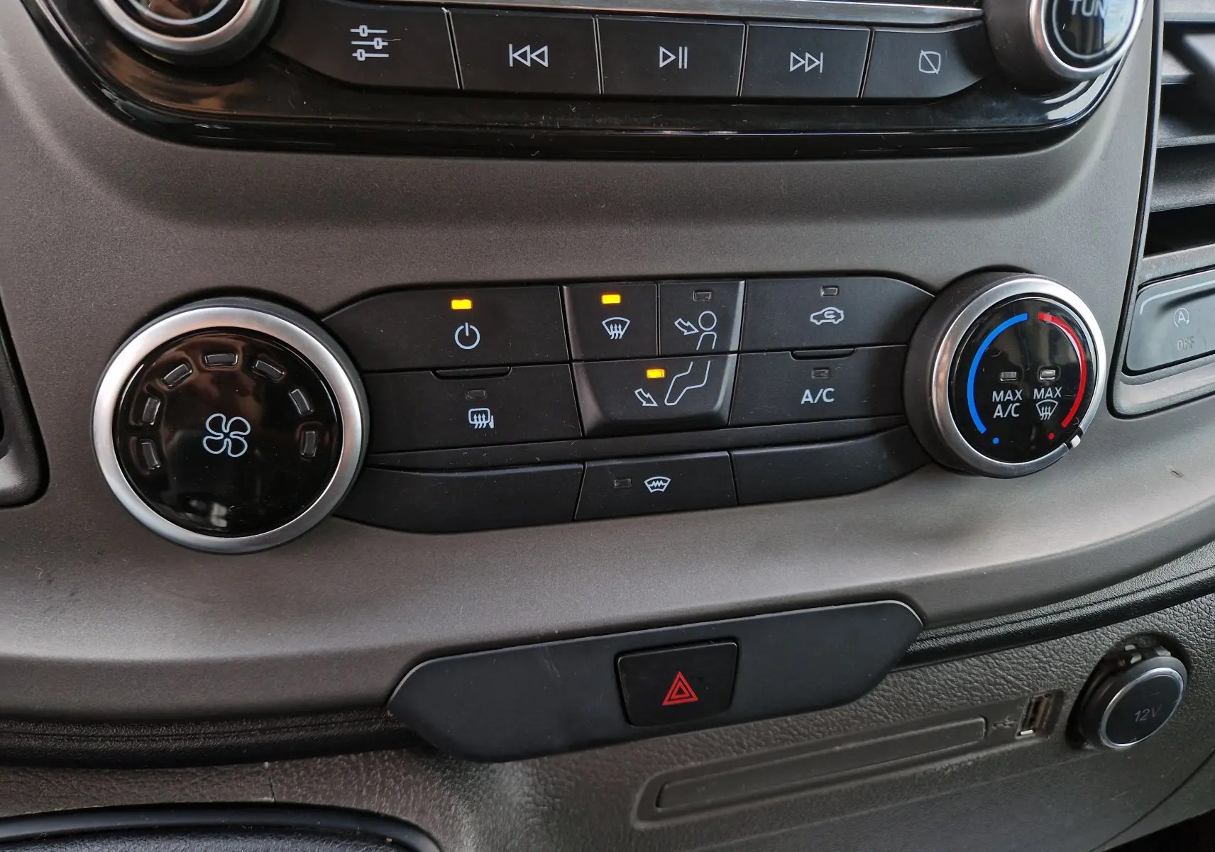 Gros plan sur la console centrale du Ford Transit Custom blanc, montrant les commandes de climatisation et de ventilation.