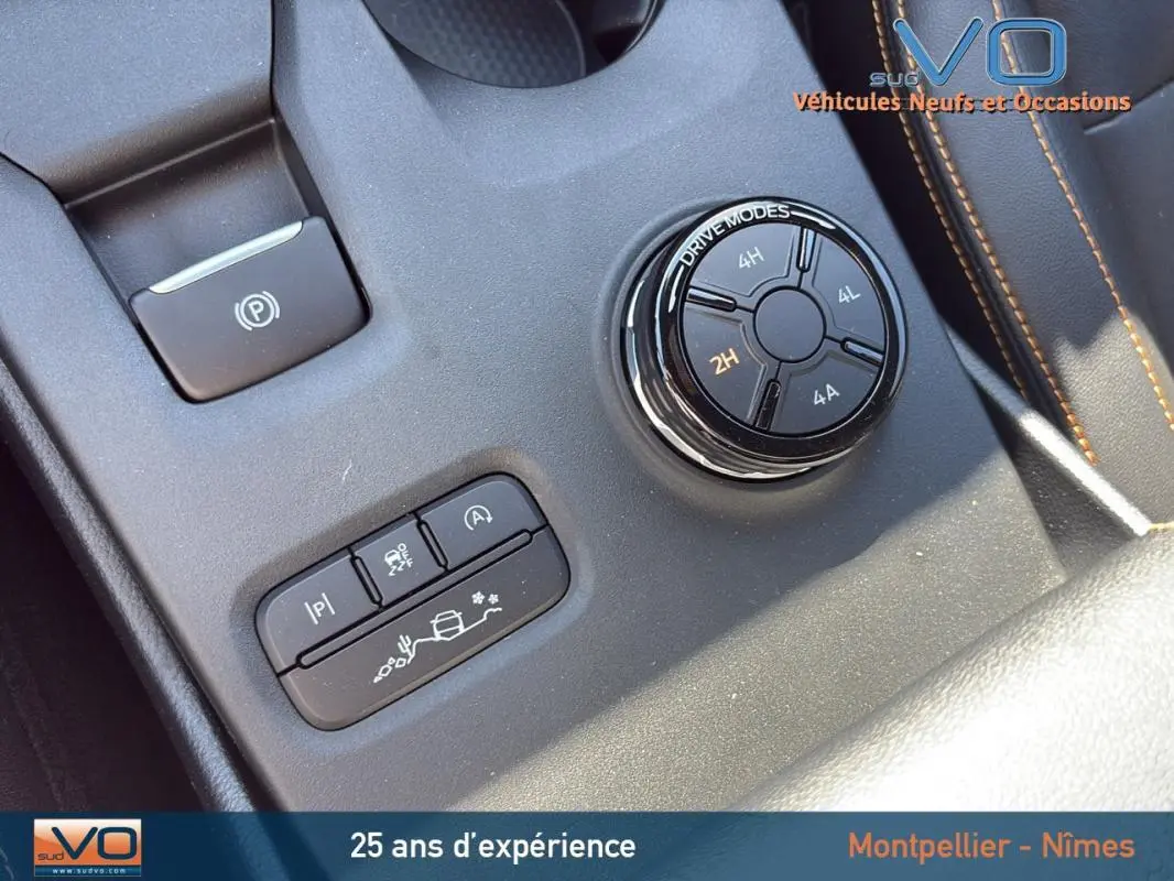 Gros plan sur la molette de modes de conduite et les boutons de contrôle du Ford Ranger Wildtrak noir, intérieur avec surpiqûres orange.