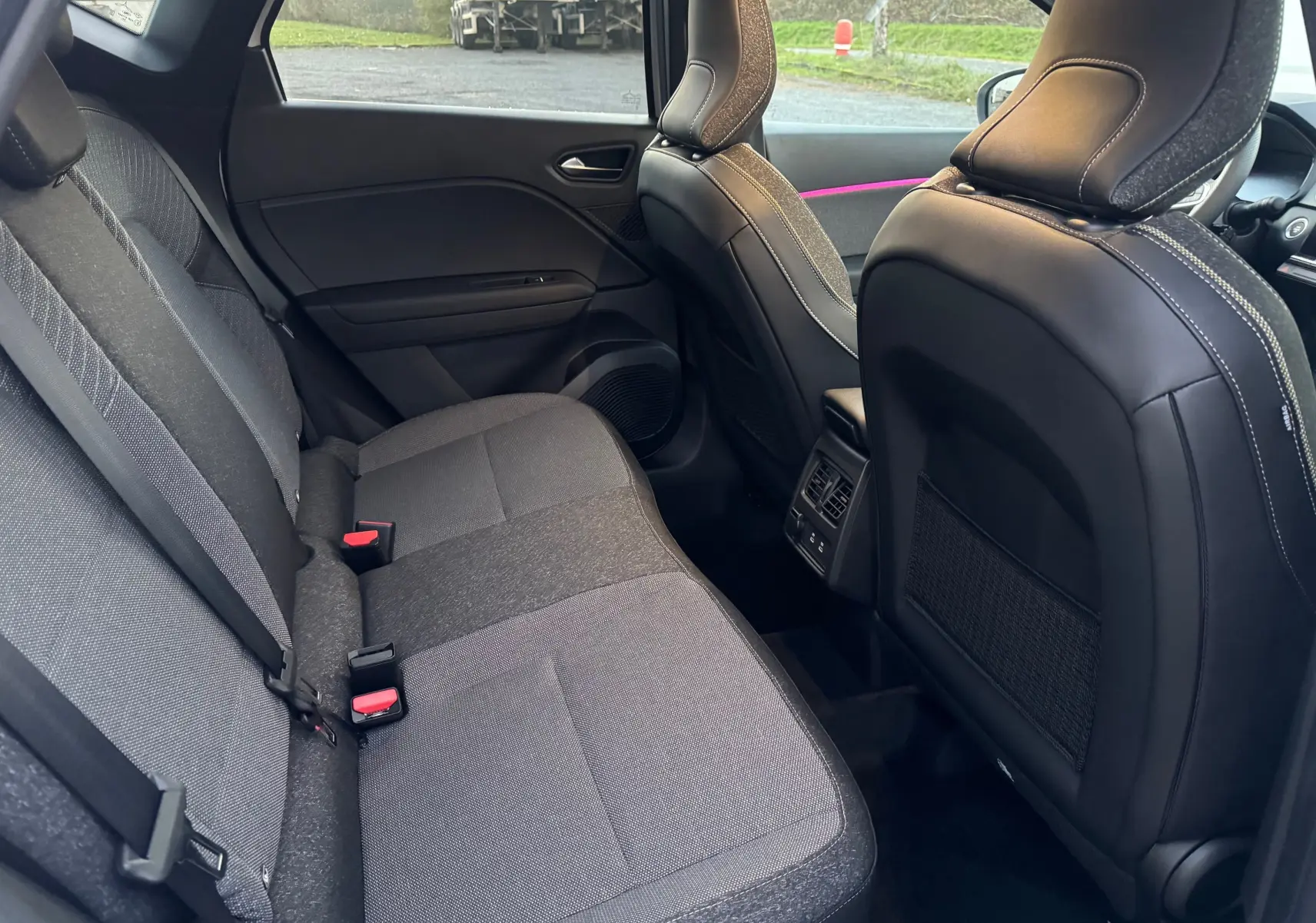 Vue intérieure arrière du Renault Captur E-Tech 2025, sièges tissu gris et dossier avant en cuir noir avec surpiqûres blanches.