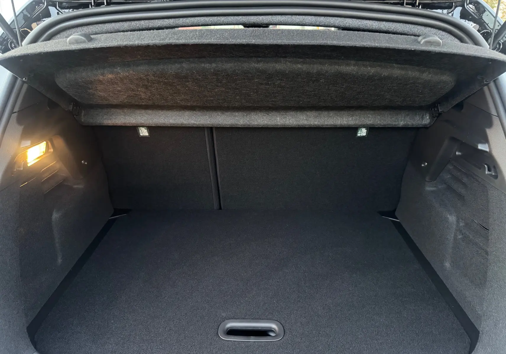 Coffre ouvert vu de l'arrière du Renault Captur E-Tech blanc nacré, intérieur noir avec éclairage latéral allumé.