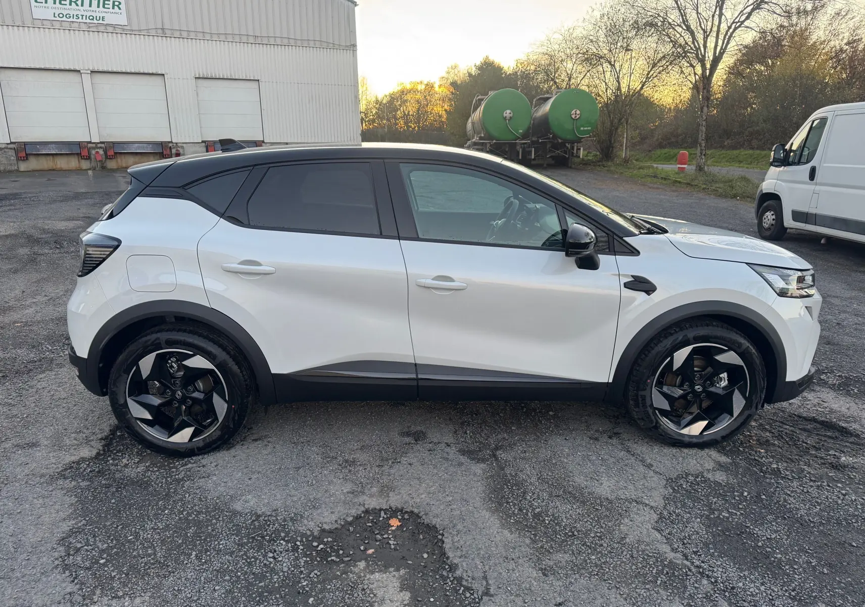 Profil côté gauche du Renault Captur E-Tech blanc nacré avec toit noir, roues noires au design moderne, sur parking extérieur.