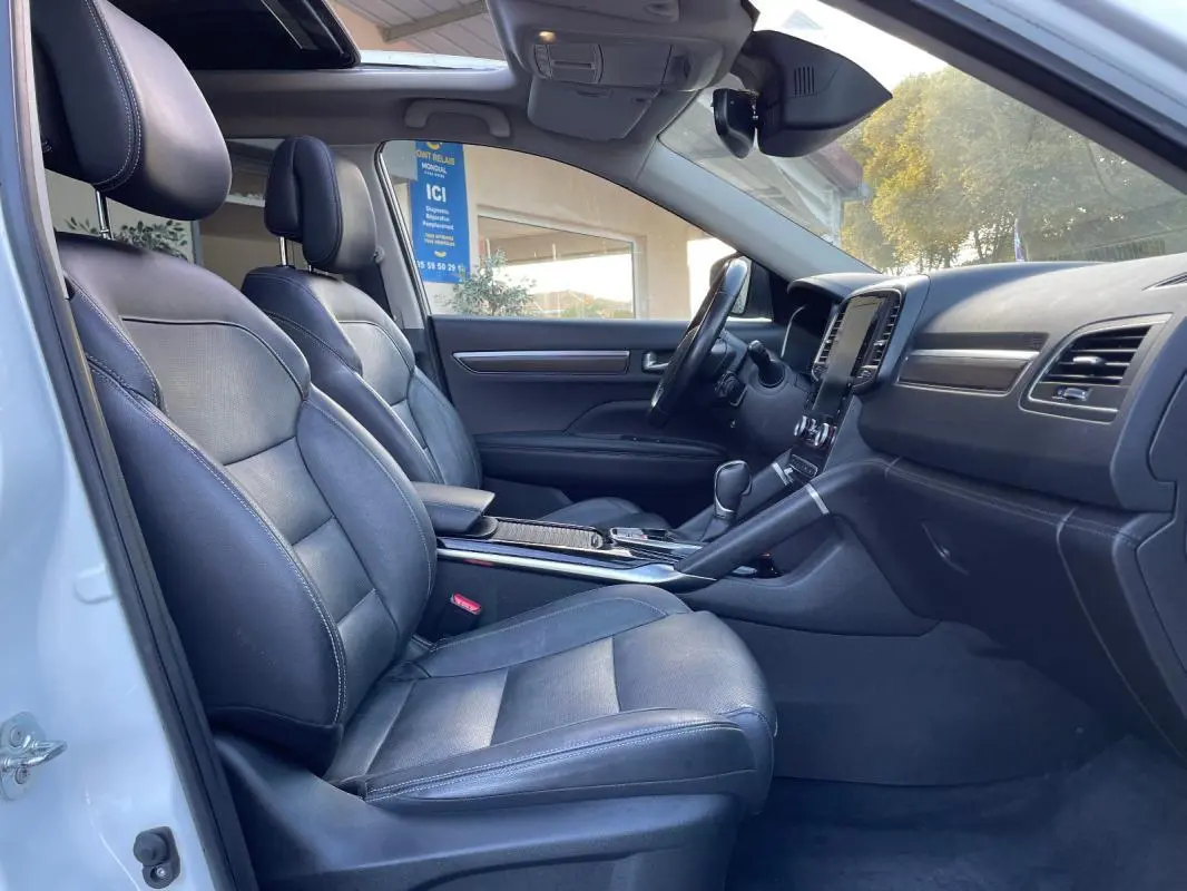 Vue intérieure côté gauche du Renault Koleos blanc 2019, sièges cuir noirs et toit ouvrant panoramique visibles.