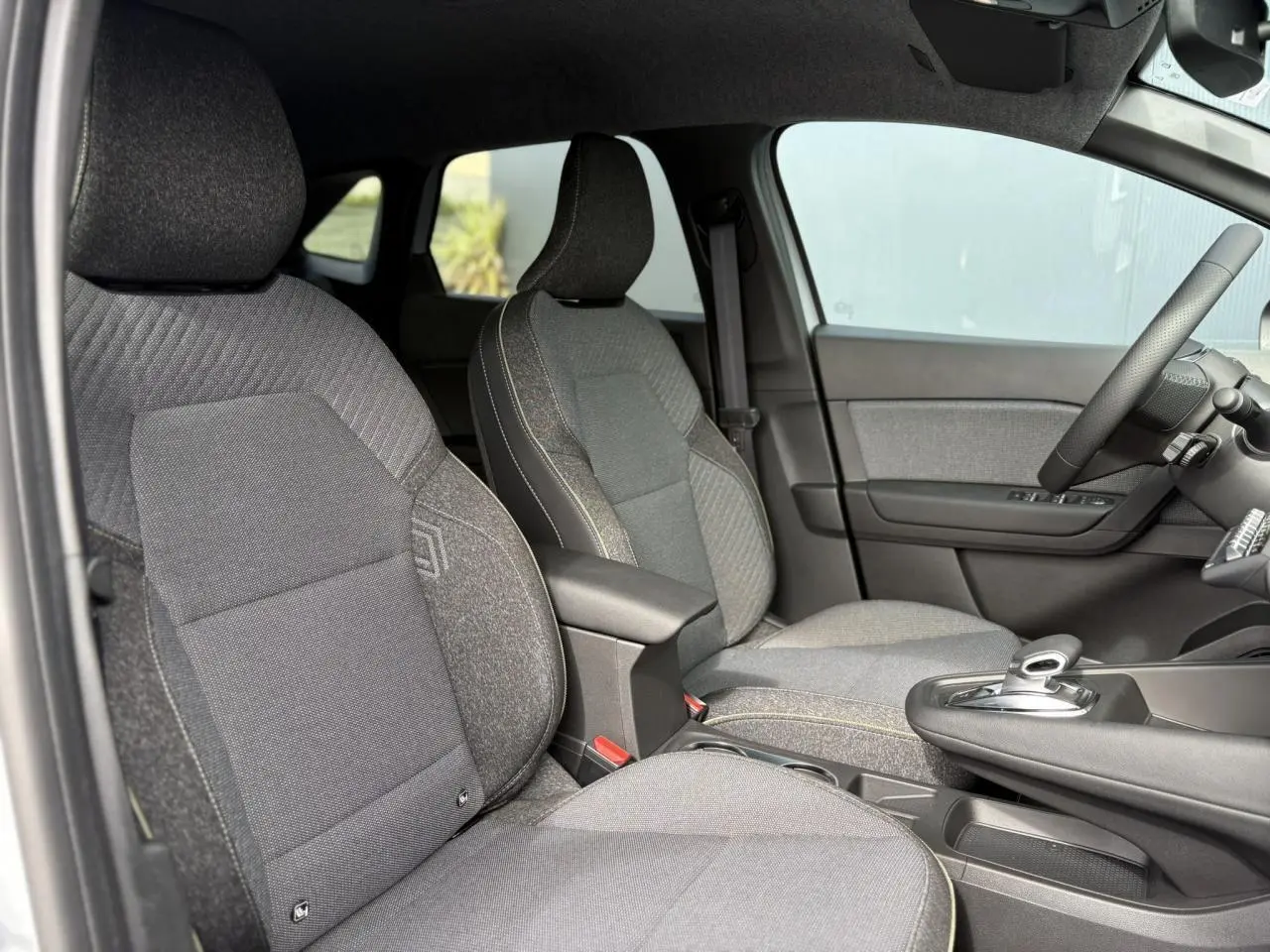 Vue intérieure côté conducteur du Renault Symbioz gris Rafale, mettant en valeur les sièges en tissu et la console centrale avec levier de vitesses automatique.