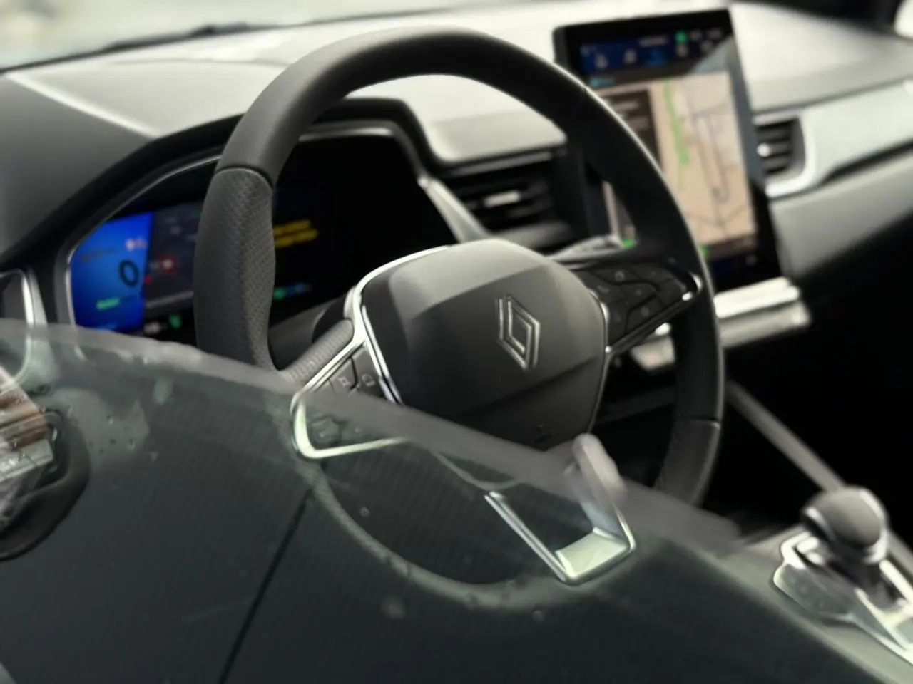 Intérieur Renault SYMBIOZ E-Tech gris, vue rapprochée du volant cuir multifonction et écran tactile central avec GPS.