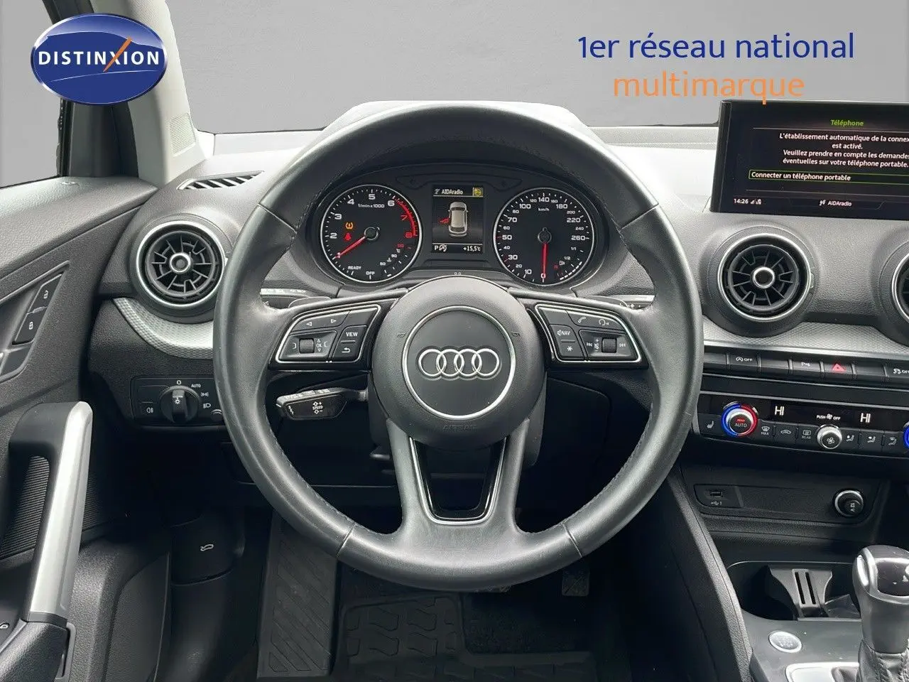 Vue intérieure centrée sur le volant Audi Q2 noir, tableau de bord avec compteurs et écran multimédia visible.