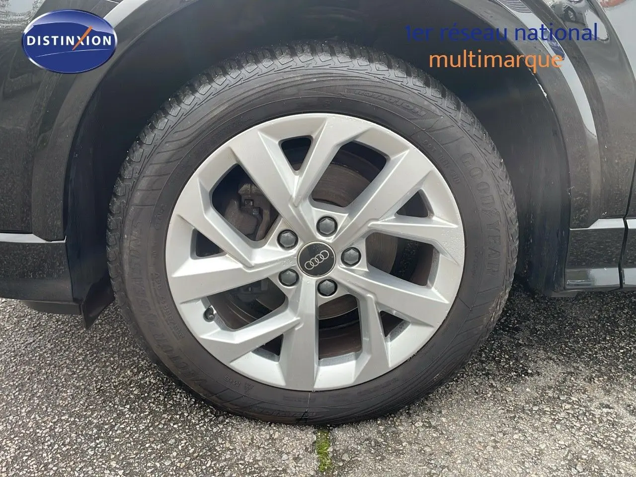 Gros plan sur la roue avant gauche d’un Audi Q2 noir mito metal, mettant en valeur la jante argentée à cinq branches.