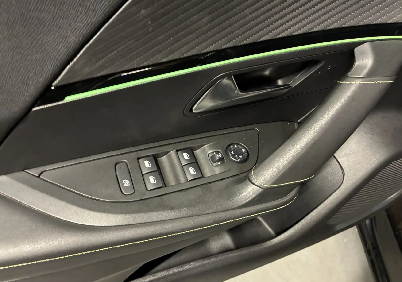 Gros plan sur la porte côté gauche du Peugeot 2008 noir, montrant les commandes des vitres et la poignée avec surpiqûres vertes.